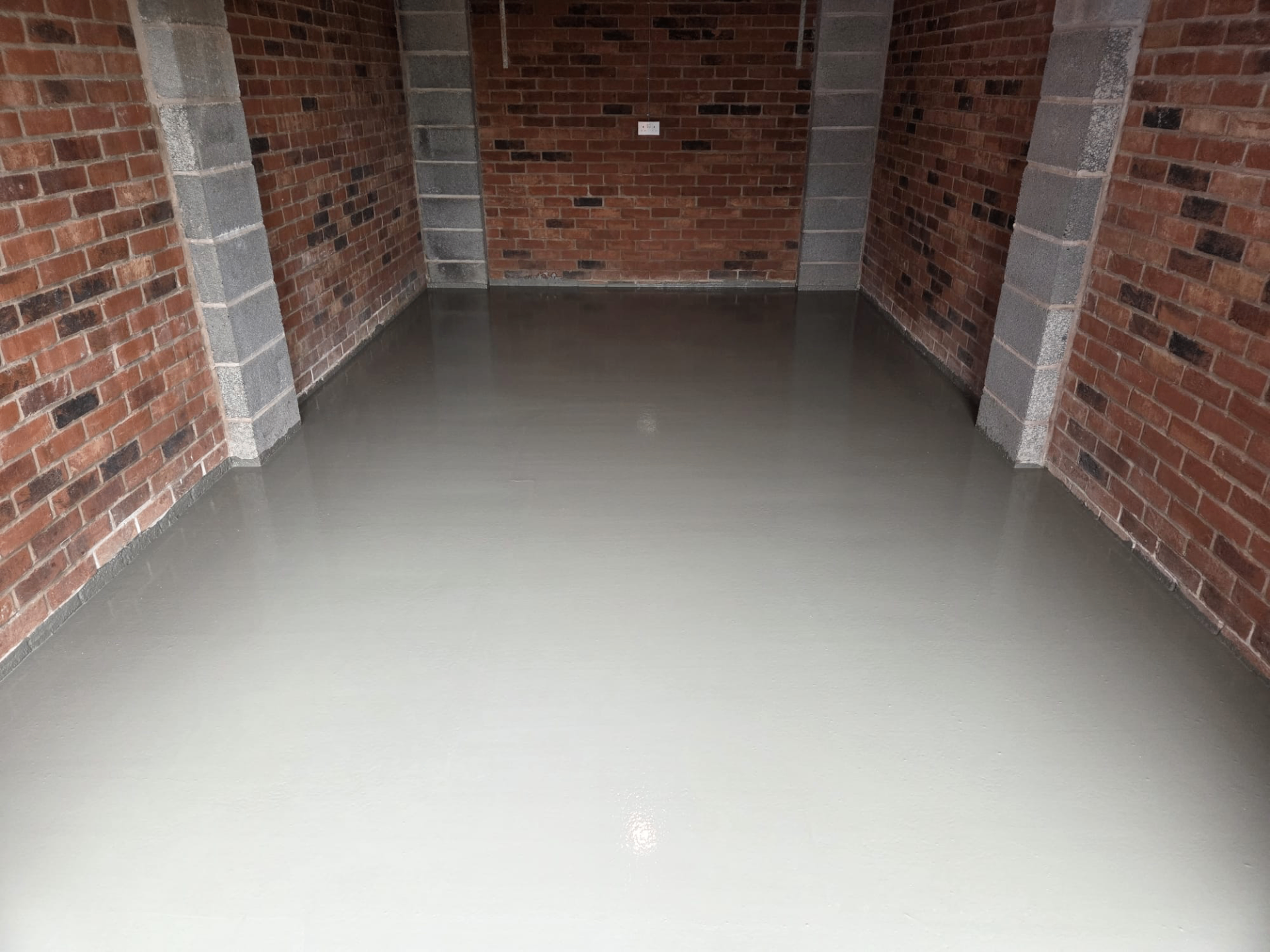 Garage screed installation finished flat between brick walls