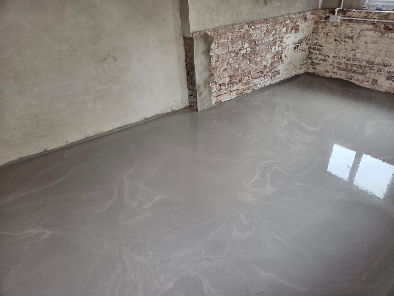 Fresh grey liquid screed in a renovation room with exposed brick